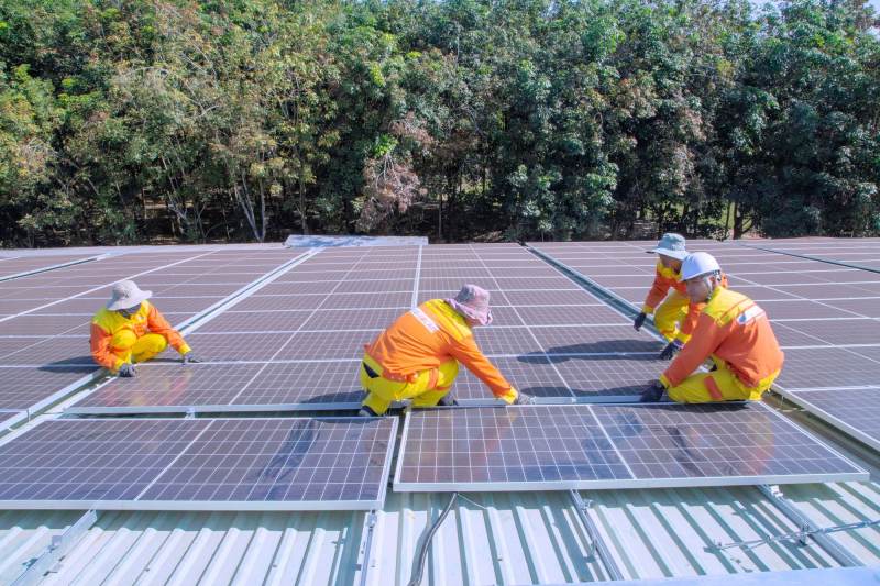 A crew in hi-vis and hard hats fitting panels on a large flat roof