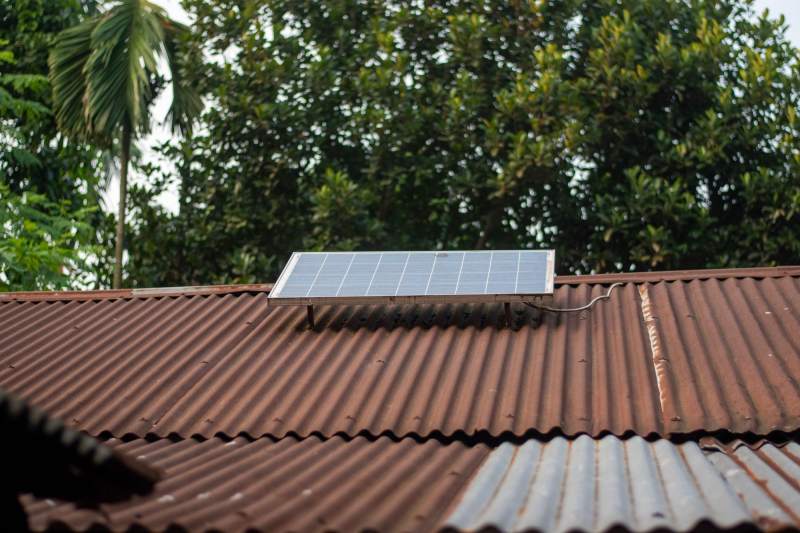 A solar panel mounted on a rusty corrugated iron roof among palm trees