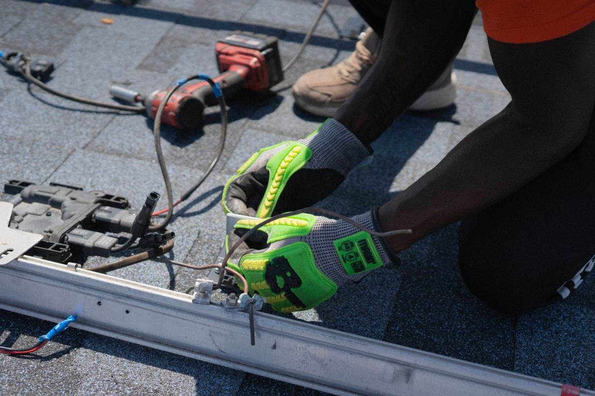 Gloved hands fixing a mounting rail on a roof with a drill
