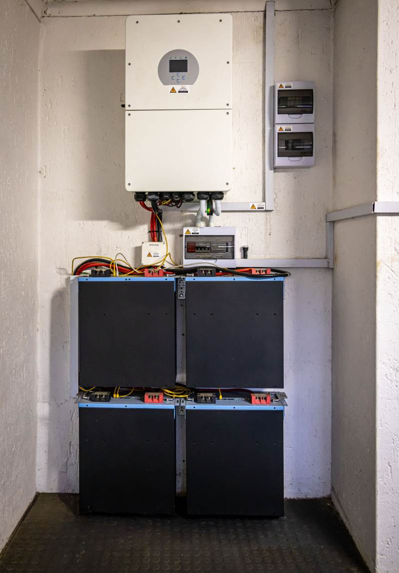An inverter mounted above a bank of batteries in a small utility cabinet