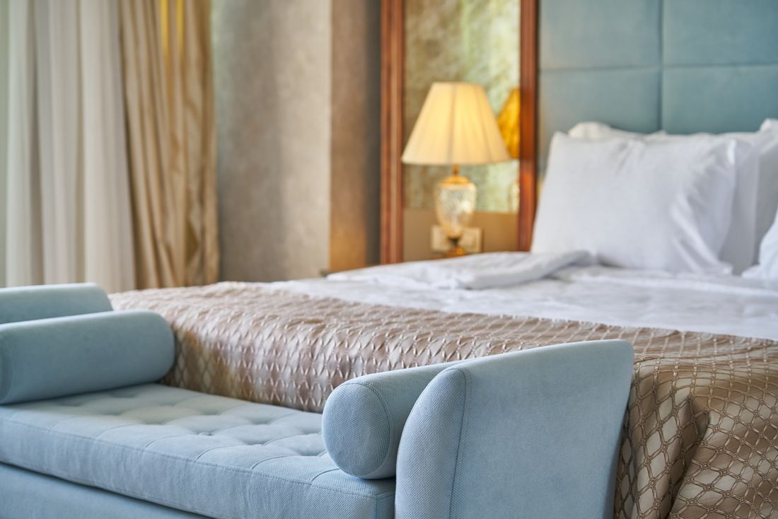 A king bed with a pale blue upholstered bench and warm lamplight