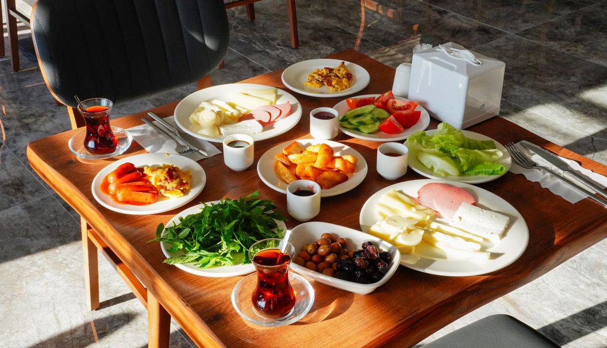 A wooden breakfast table laid with fresh dishes, salads, cheese and tea