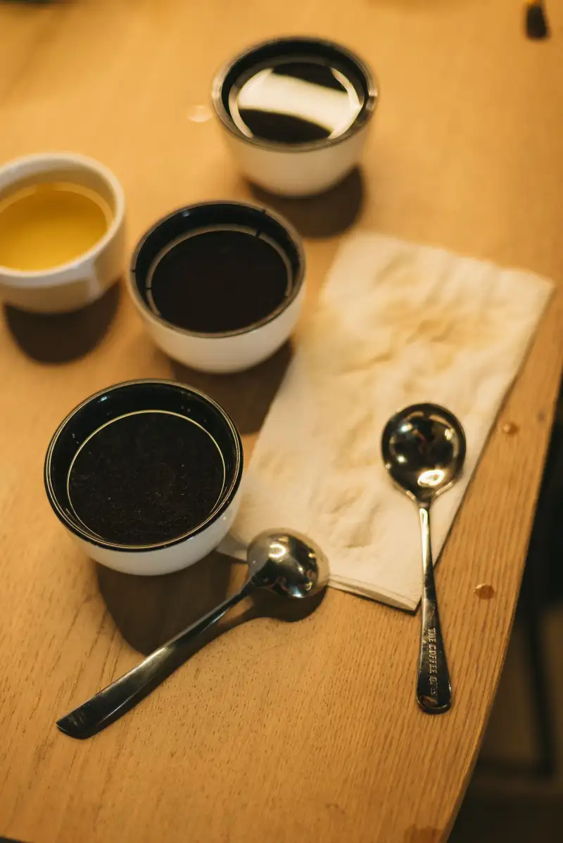 Cupping bowls of ground coffee on a wooden table with tasting spoons