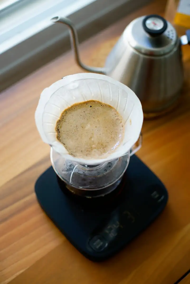 Coffee being brewed through a paper filter on a scale, with a gooseneck kettle behind
