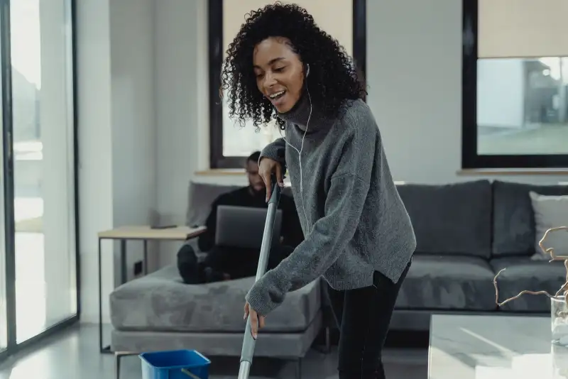 A woman mopping the floor of a bright living room while music plays in her earphones