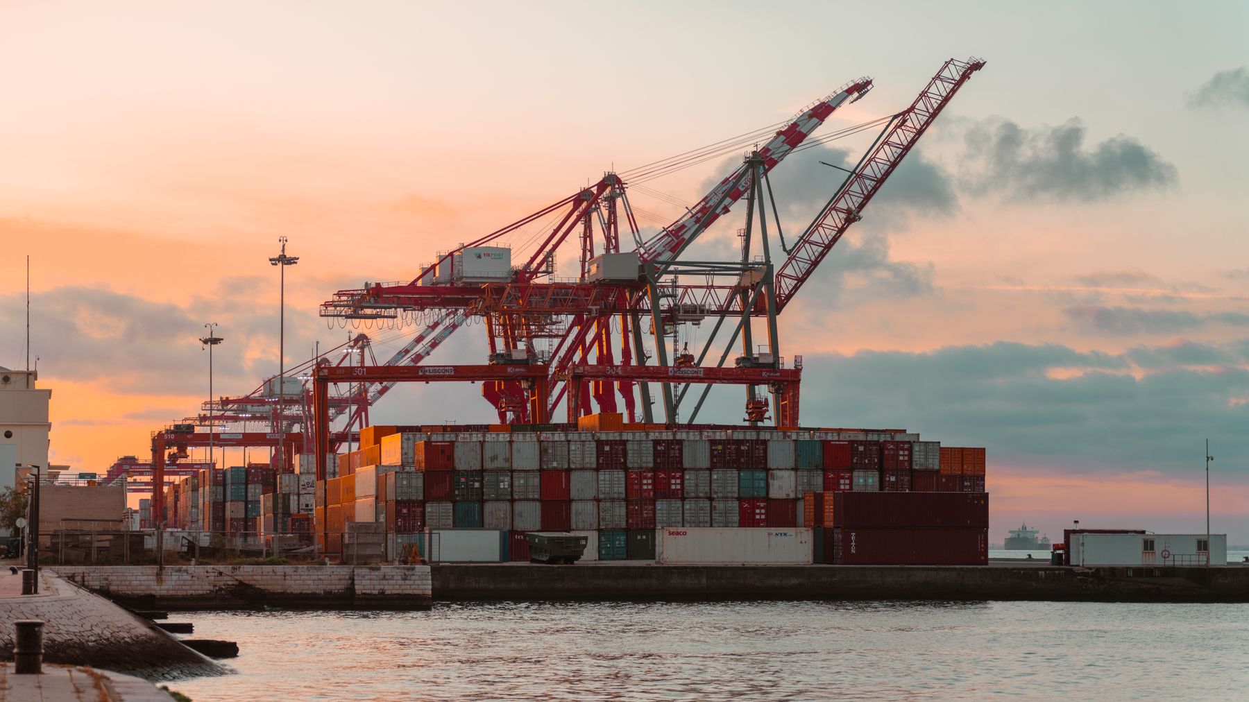 Shipping cranes loading a container vessel at an industrial port at sunset