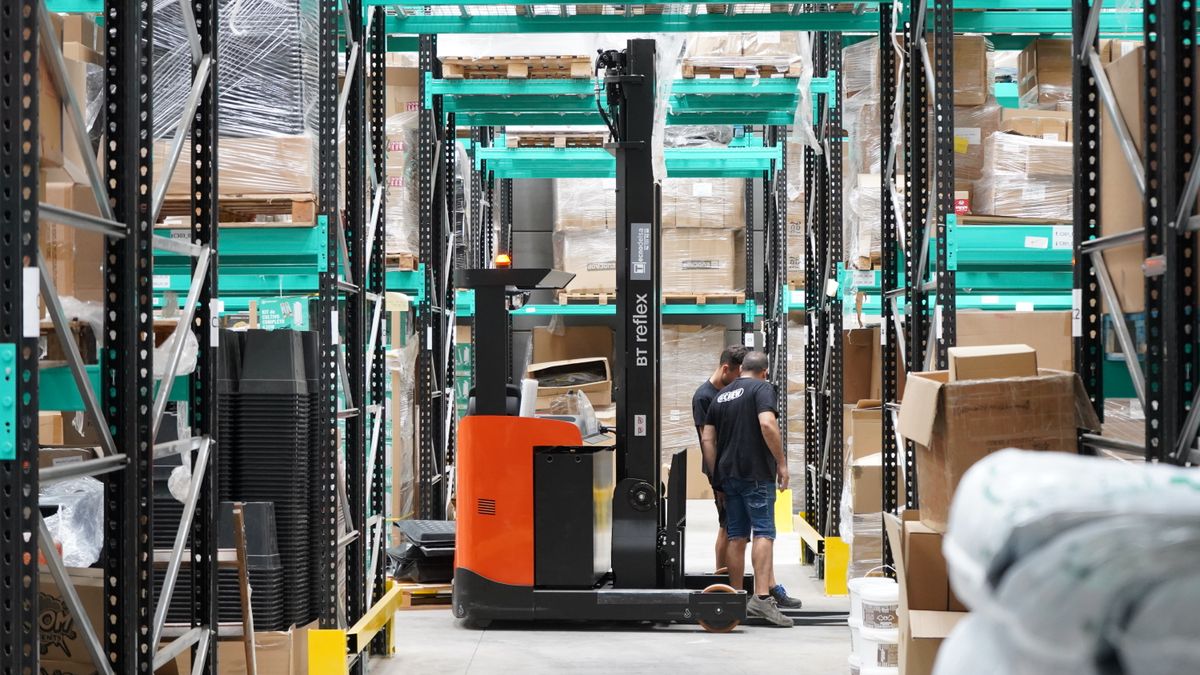 Warehouse staff operating a forklift among stacked pallets of goods