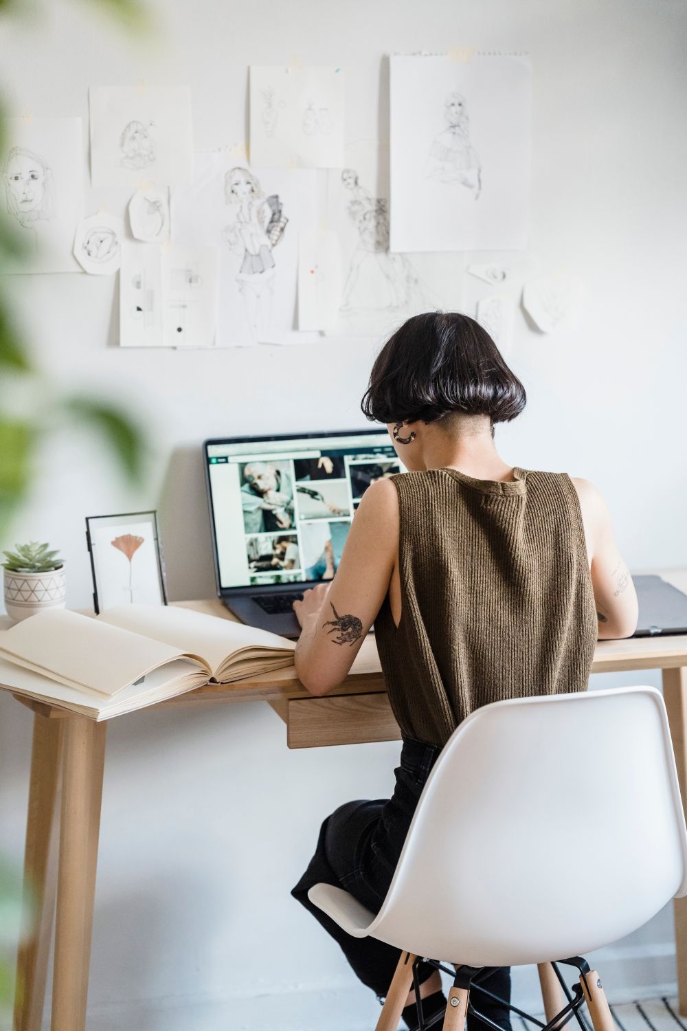 A designer seen from behind sitting at a light wooden desk with sketches pinned on the wall