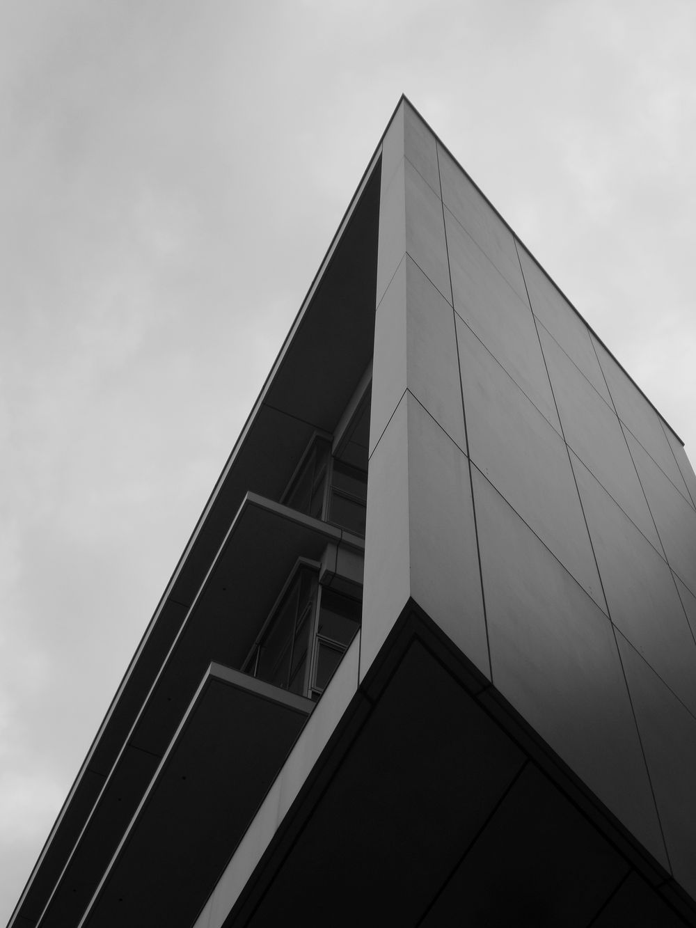 A black and white photograph of an angular building corner against a cloudy sky